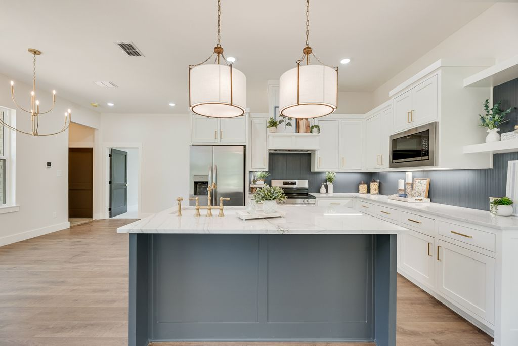 Modern kitchen with gray island, white cabinets, and two pendant lights.