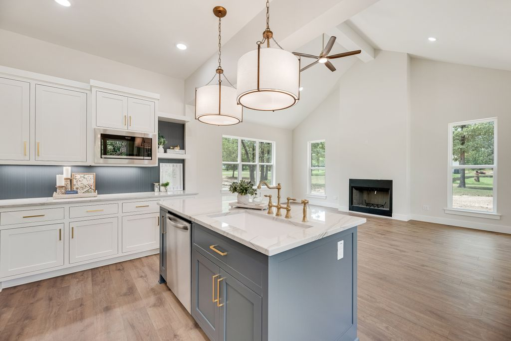 Open-plan kitchen with blue island, white cabinets, and pendant lights.  A fireplace is in the background.
