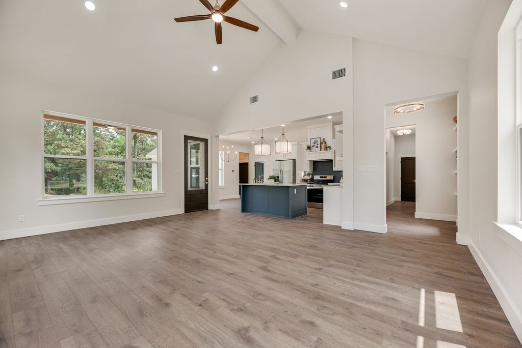 Spacious, modern living room with wood floors, white walls, large windows, and blue kitchen island.