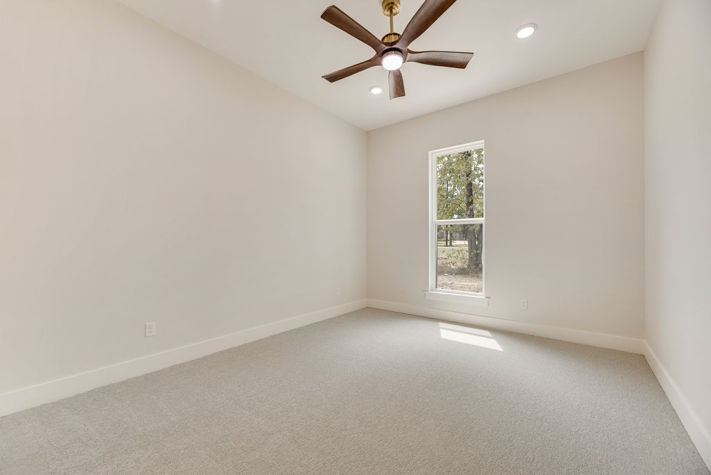 Empty room with light gray carpet, white walls, window, and ceiling fan.