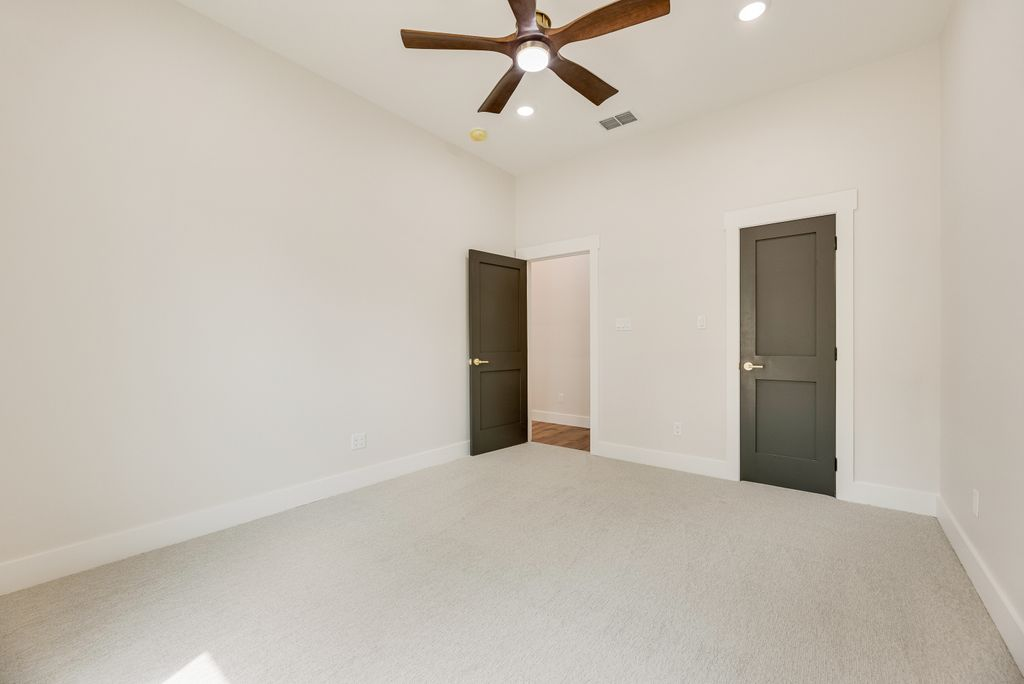 Empty room with beige carpet, white walls, dark green doors, and a ceiling fan.