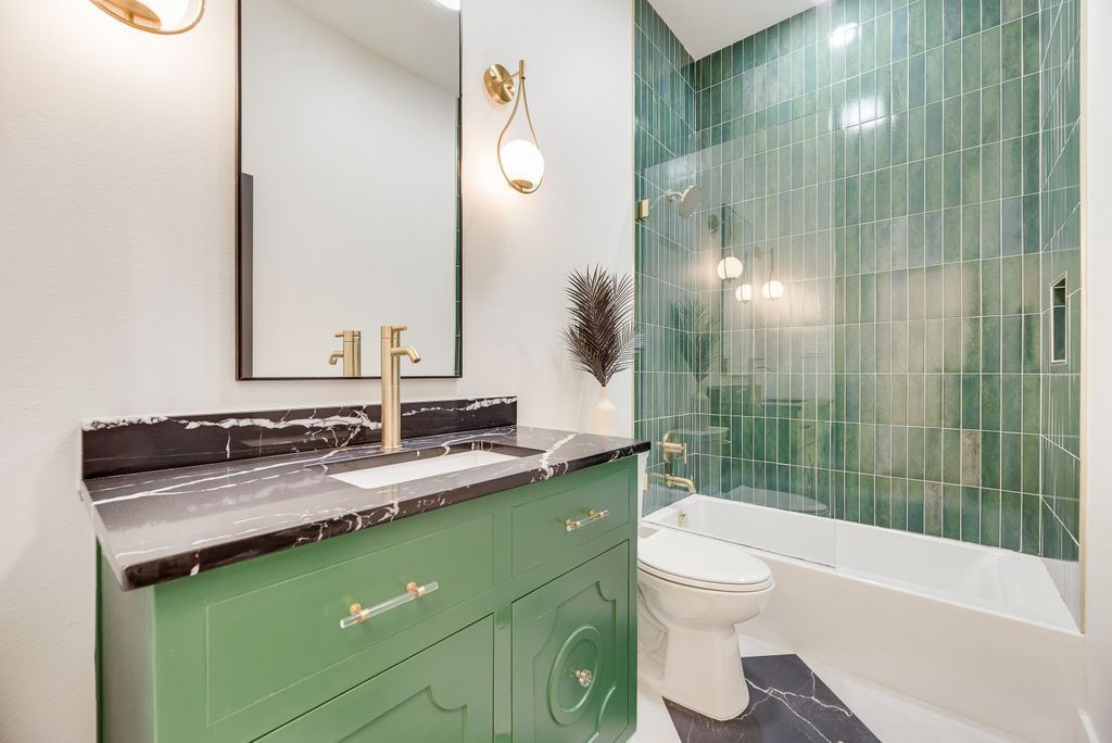 Green bathroom with green vanity, black countertop, green tile shower and gold fixtures.