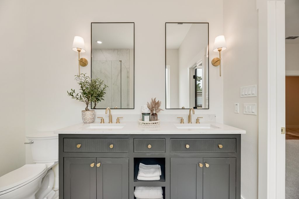 Bathroom vanity with gray cabinets, white countertop, two mirrors, and gold fixtures.