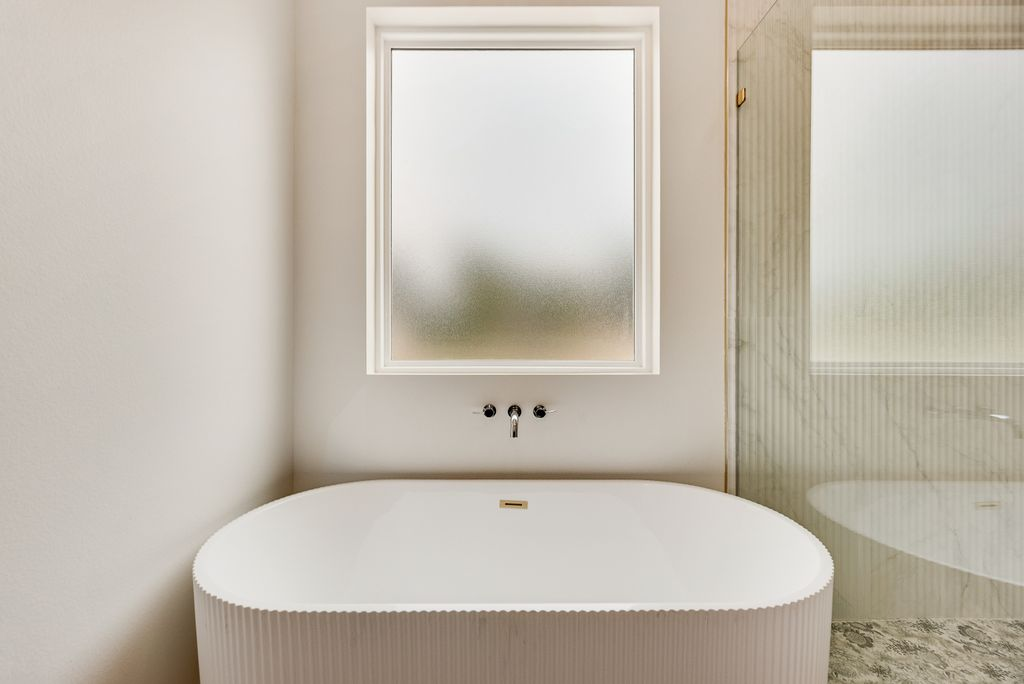 Modern bathroom with a white oval bathtub under a frosted window.