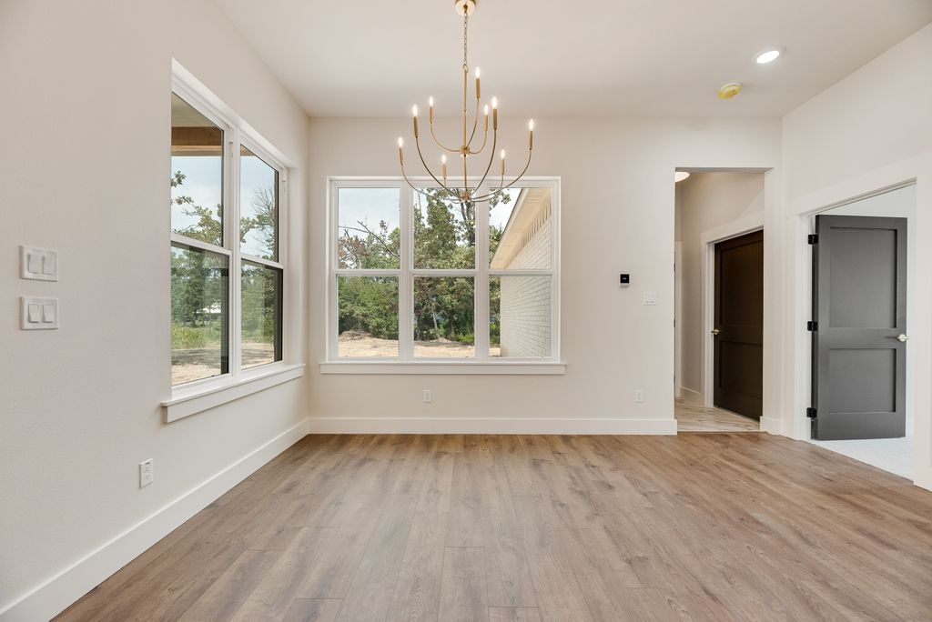 Empty dining room with chandelier, large windows, and wood floors.