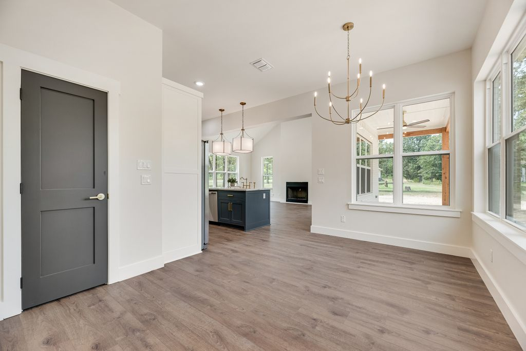 Interior of a home with gray door, wood floors, and a view into the kitchen and living area with a chandelier.