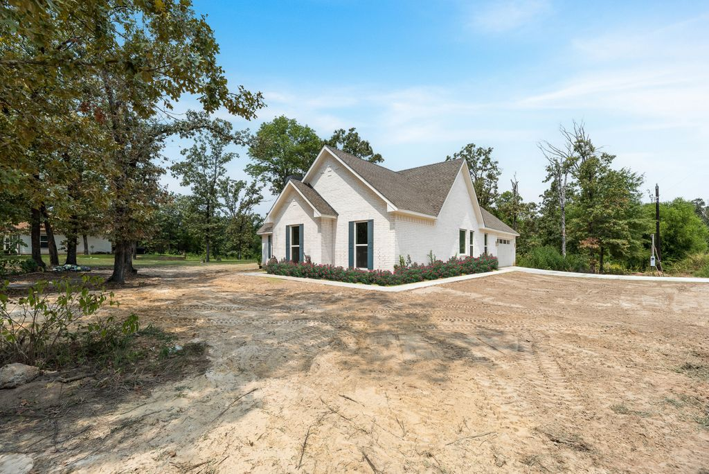 White brick house with dark shutters, brown roof, and landscaping under a blue sky.