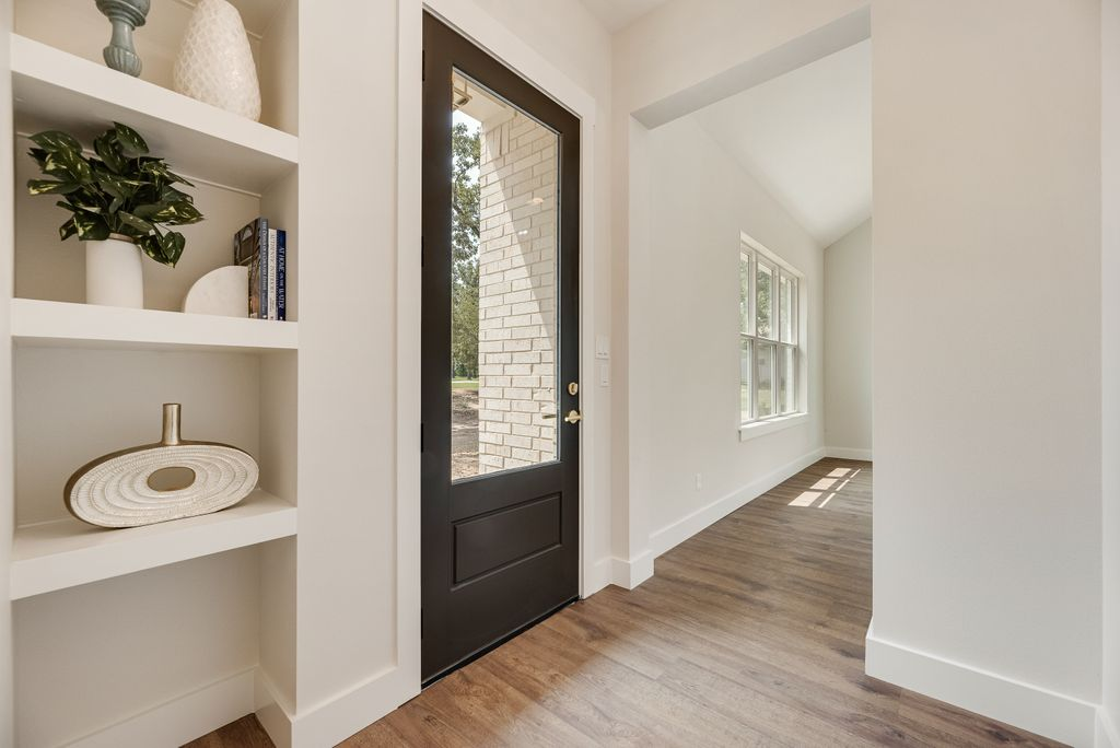 Entryway with a black door, built-in shelves with decor, and wood flooring.