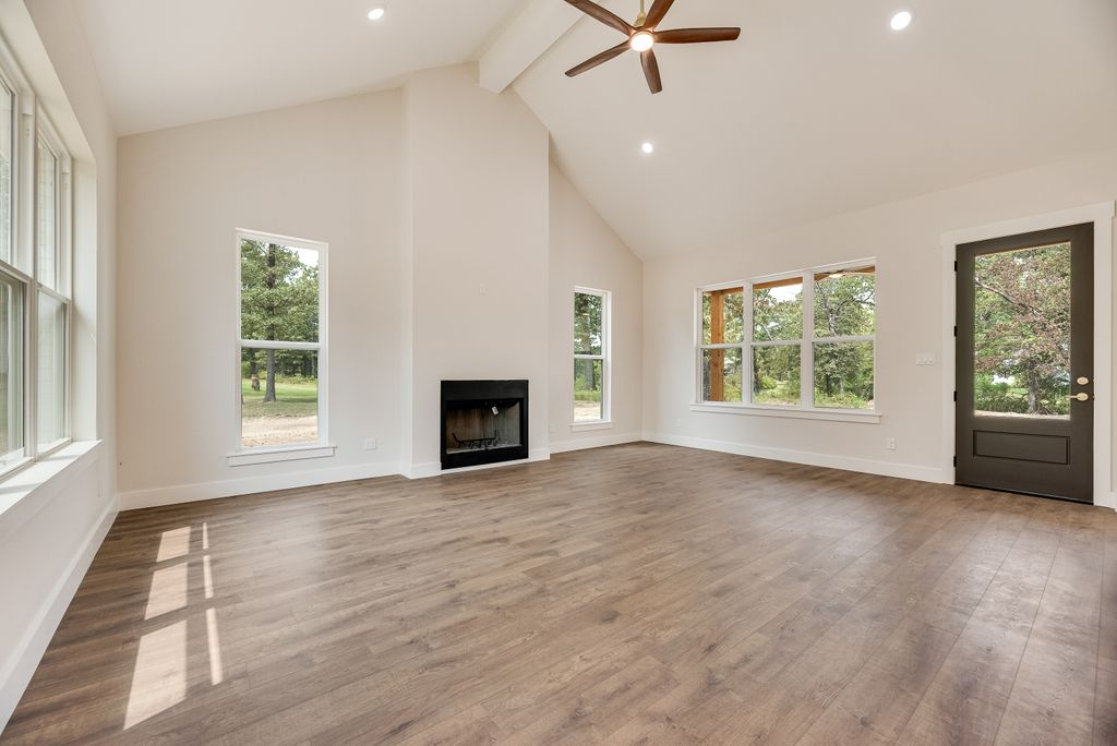 Empty living room with fireplace, high ceiling, hardwood floors, and windows.