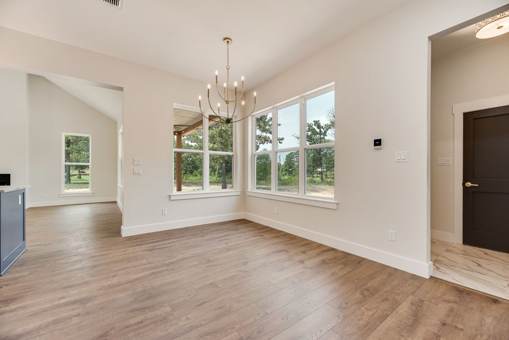 Light-filled interior with wooden floors, large windows, and a chandelier. Doorway and light switch are visible.