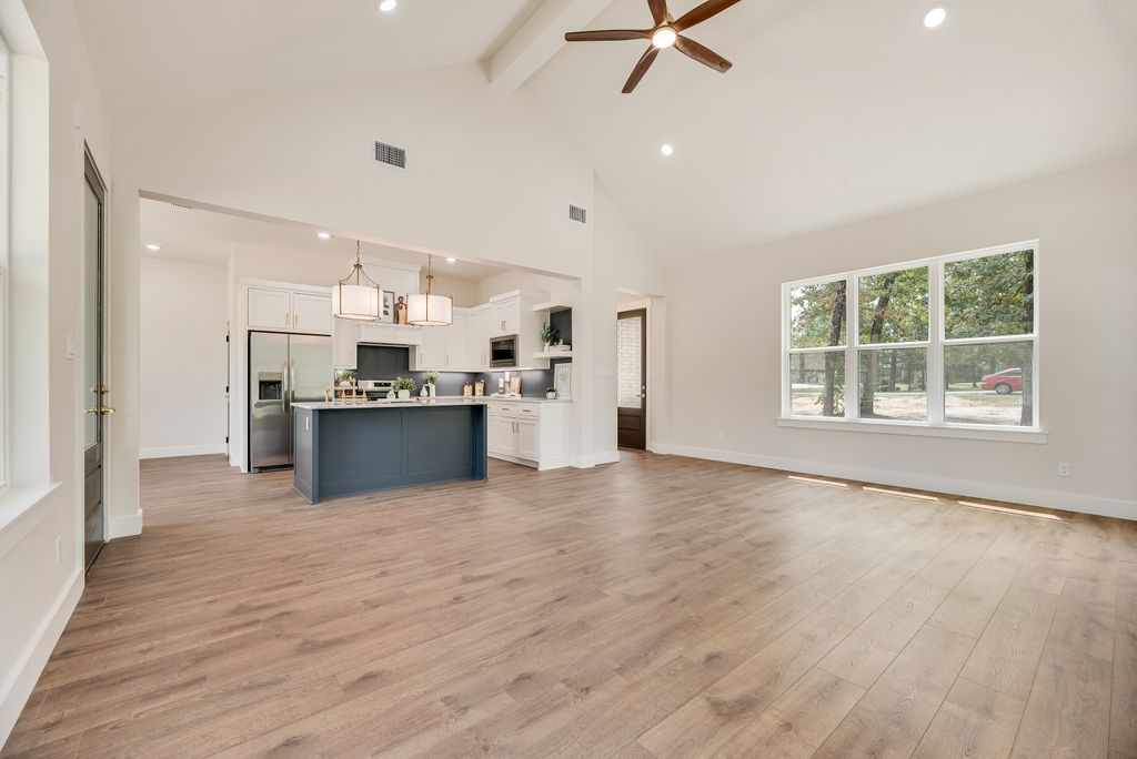 Open-concept living space with wood floors, kitchen island, and large windows overlooking trees.