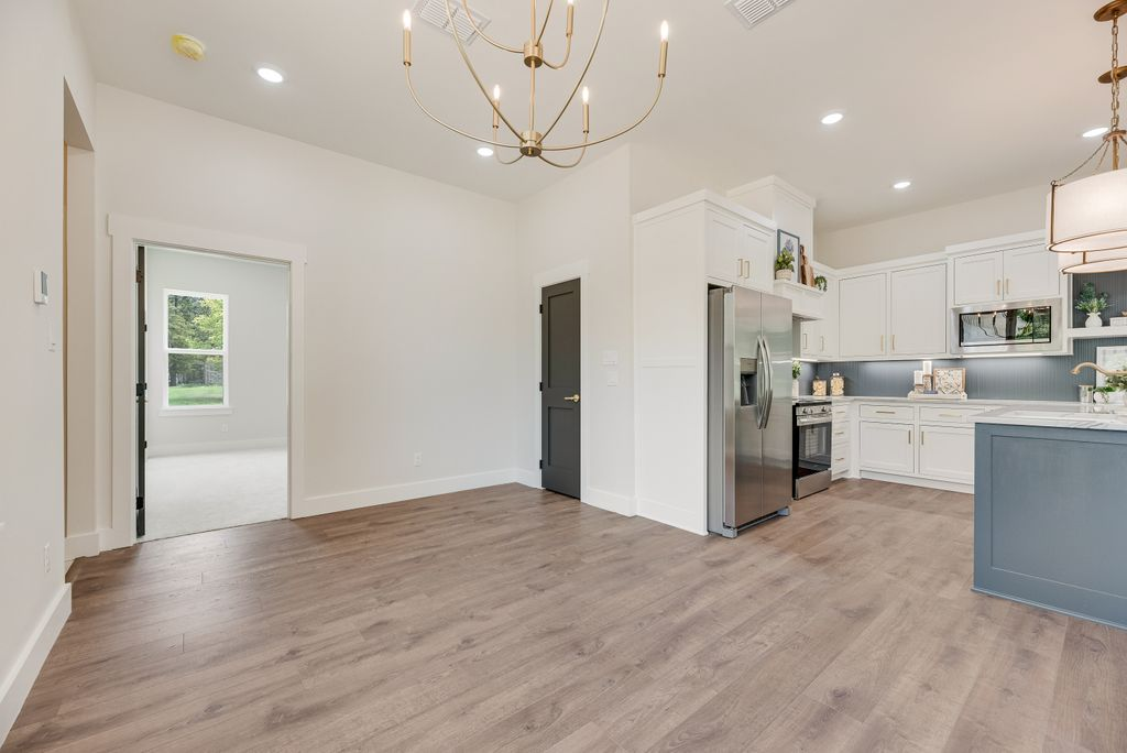 Open kitchen with wooden floors, white cabinets, stainless steel appliances, and an open doorway.