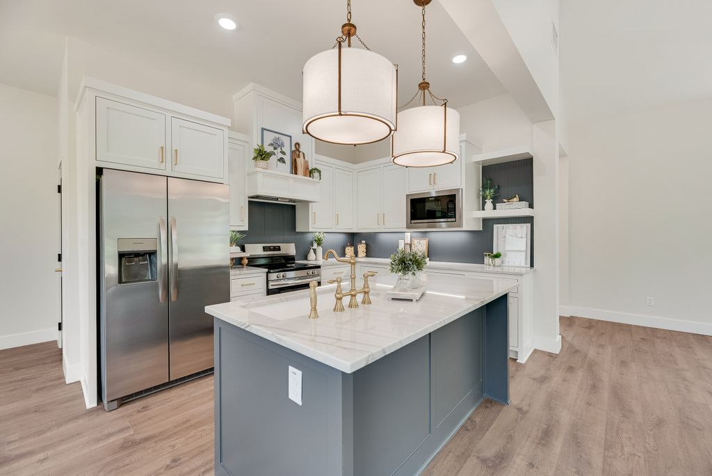 Modern kitchen with gray island, white cabinets, stainless steel appliances, and light wood floors.