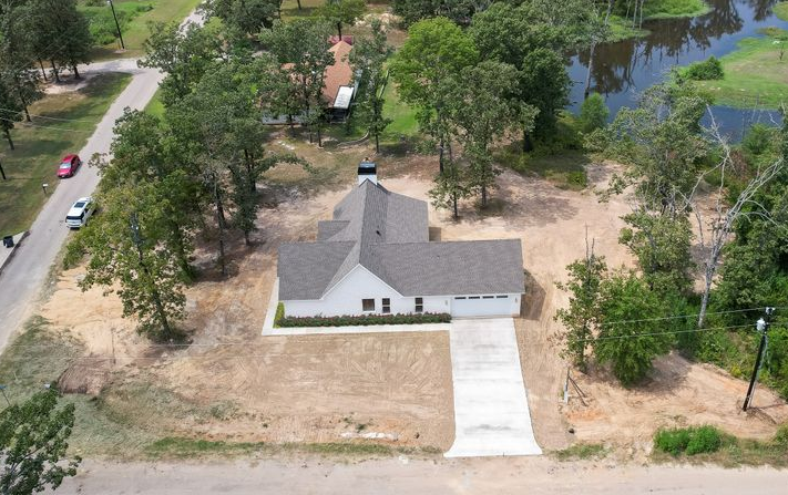 Aerial view of a white house with a gray roof and long driveway, surrounded by trees and a body of water.