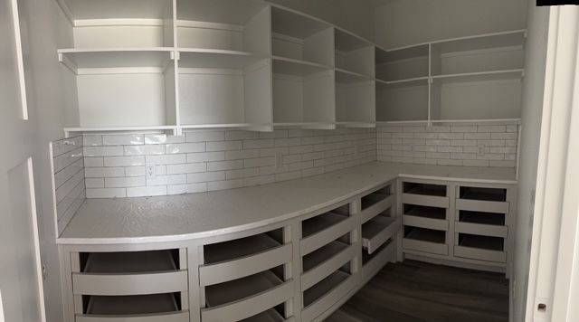 White pantry with empty curved lower cabinets, shelves above, and subway tile backsplash.