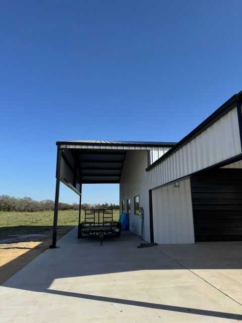 Black and white metal building with a covered area; blue sky in the background. Trailer parked underneath.