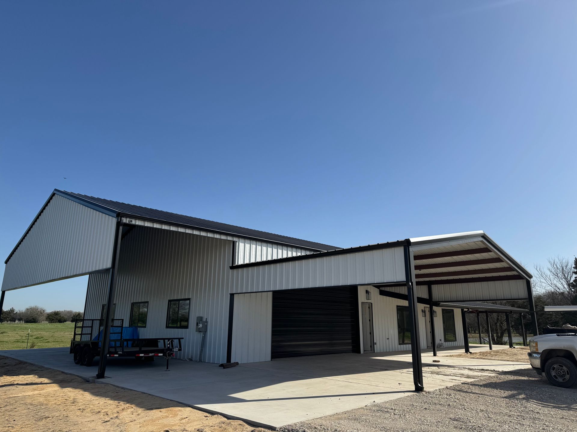 Metal barn with a carport, on a concrete pad, under a clear blue sky.