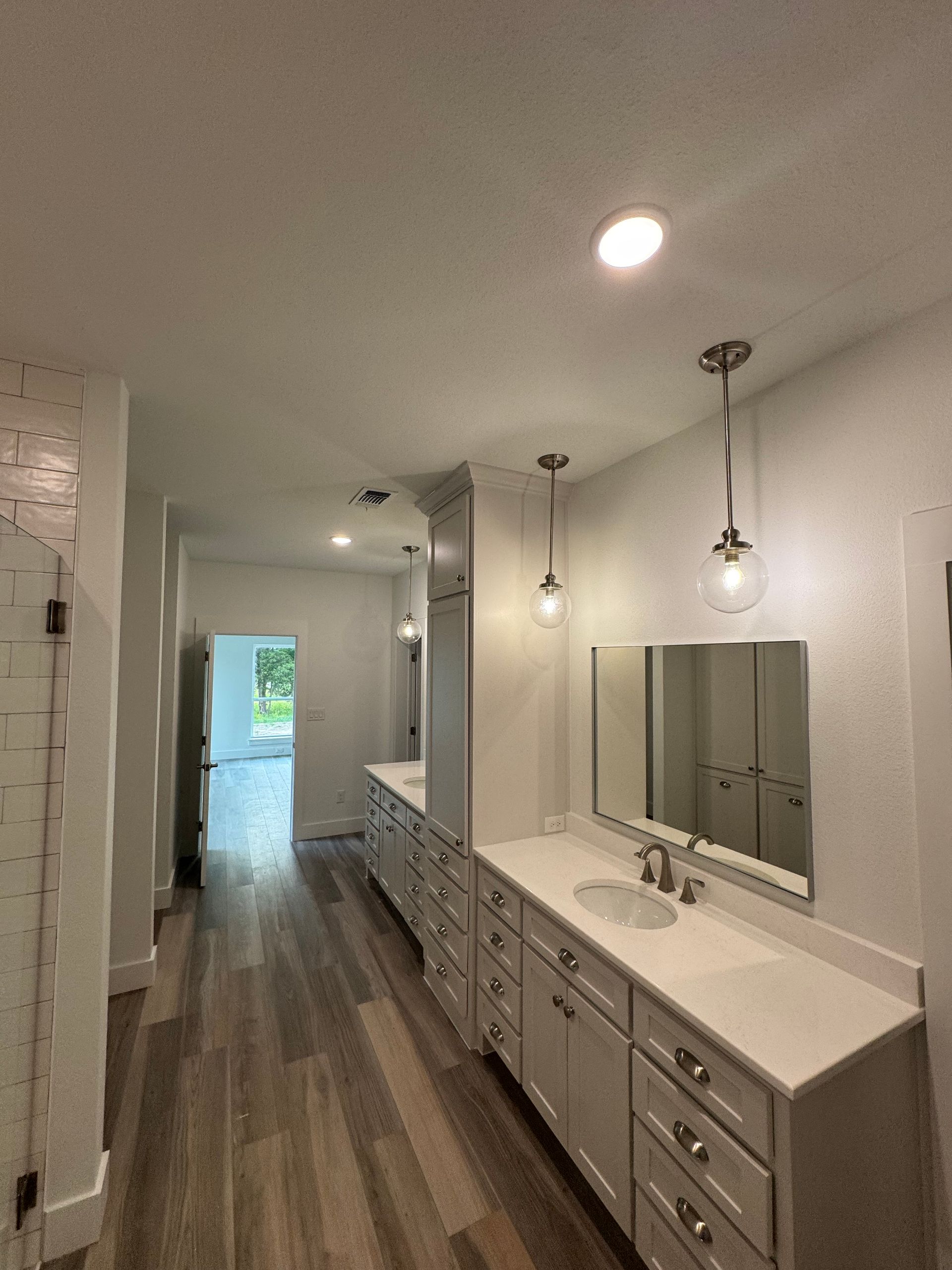 Spacious modern bathroom with dual vanity, white cabinets, wood floors, and pendant lighting.
