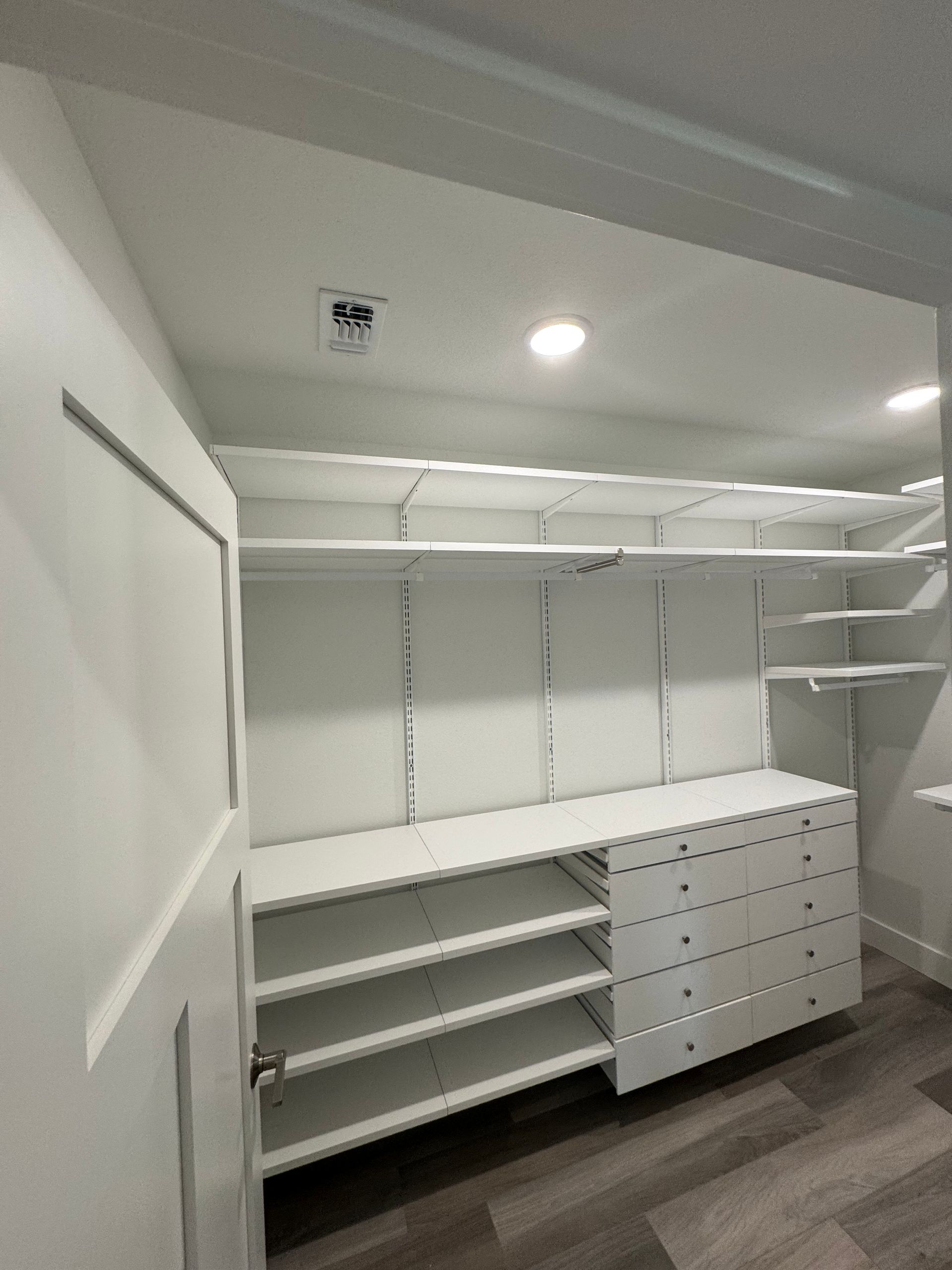 White walk-in closet with shelves, drawers, and a door.