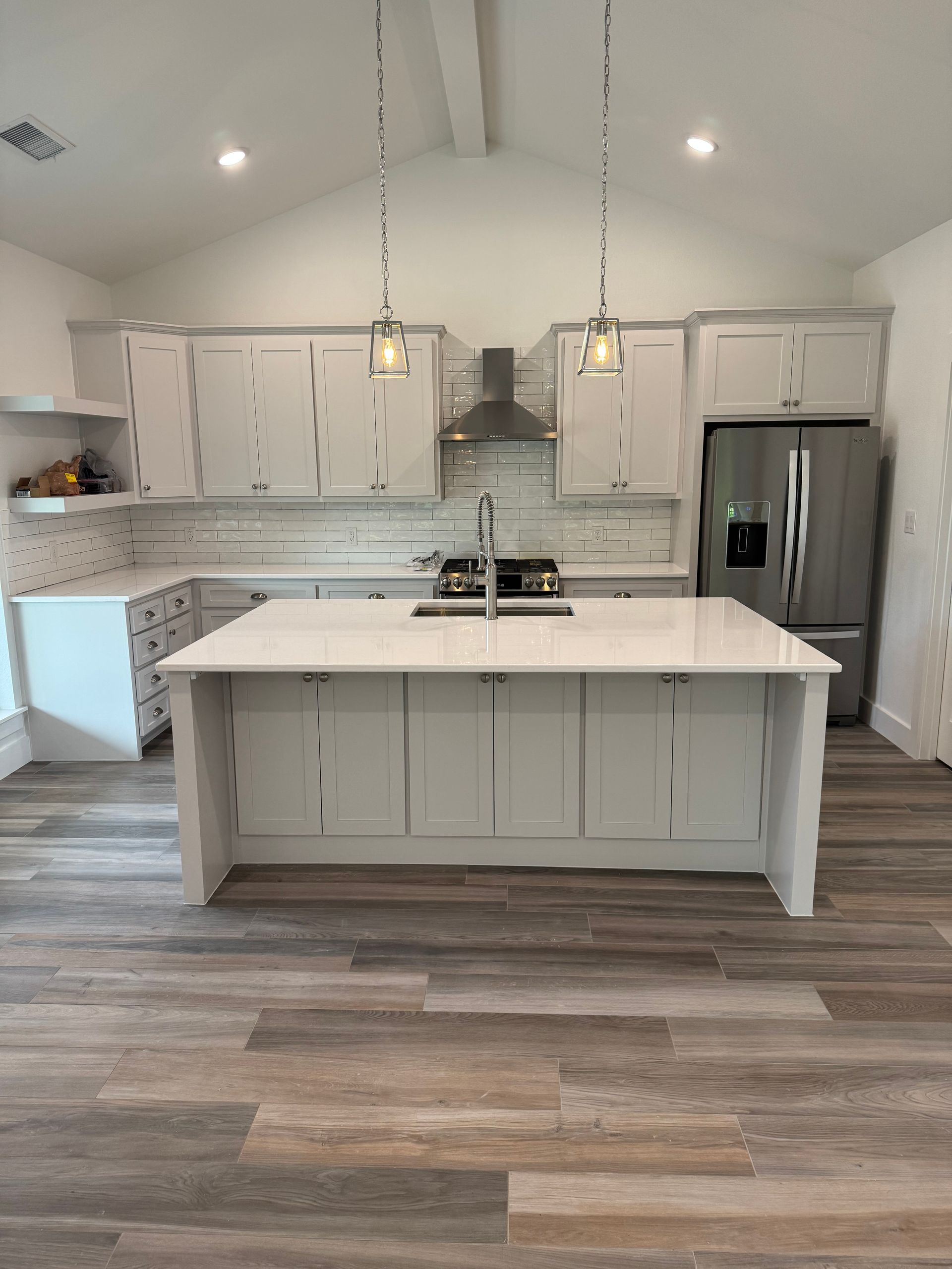 Modern kitchen with gray cabinets, island, stainless steel appliances, and wood-look flooring.