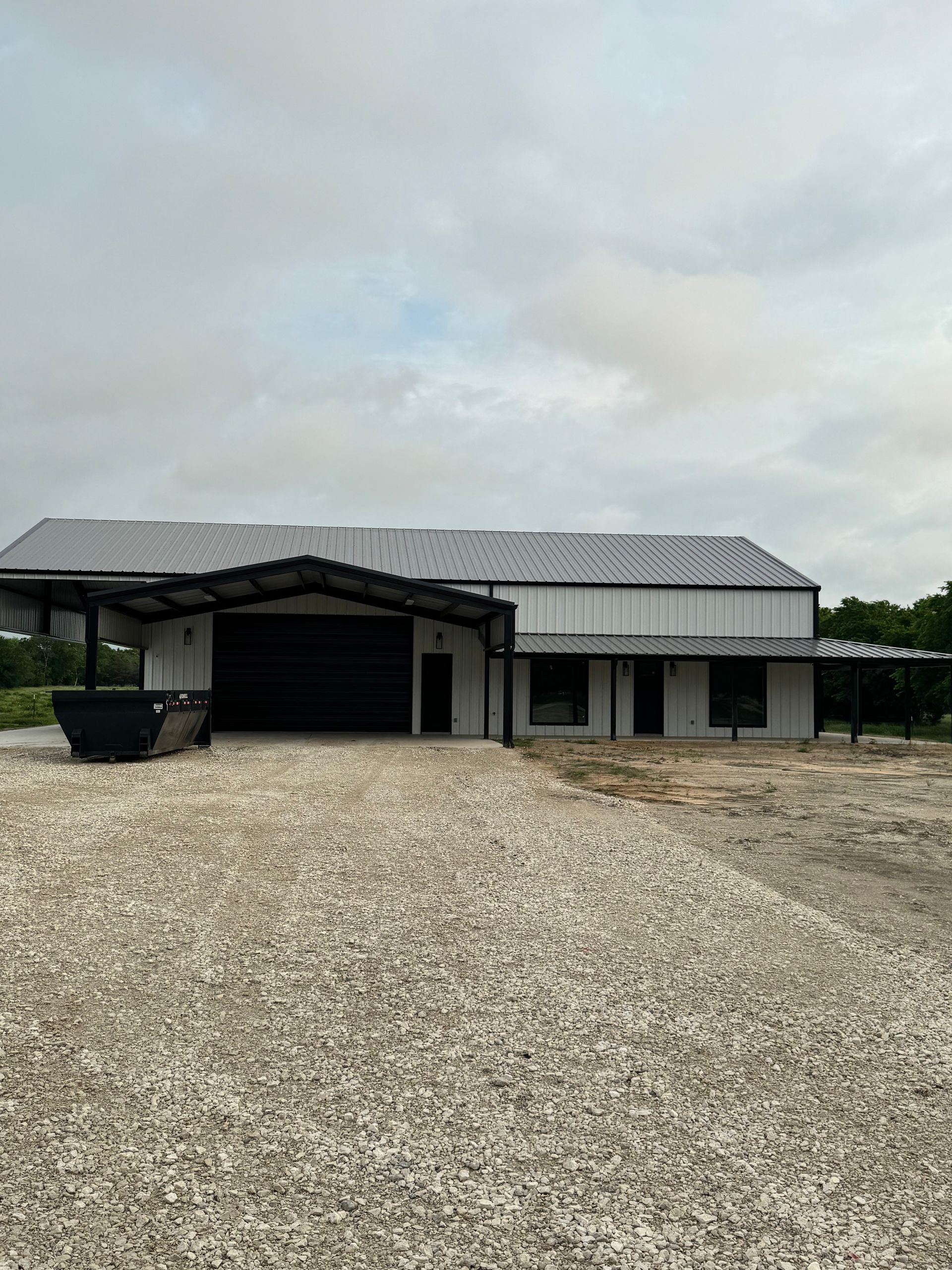 White building with black accents, a gray gravel driveway, and an overcast sky.