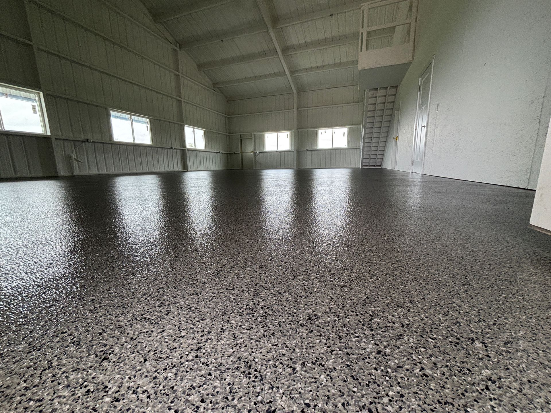 Dark speckled floor in a large, empty industrial building with windows and high ceilings.