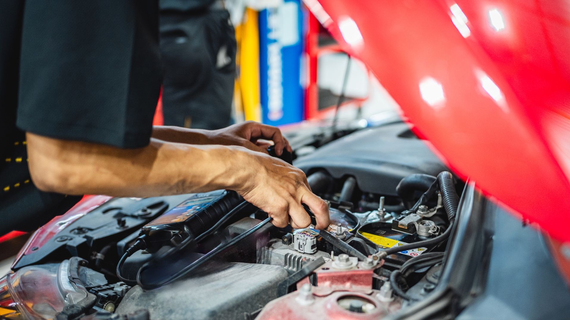 Mechanic working on a car engine with the hood open.