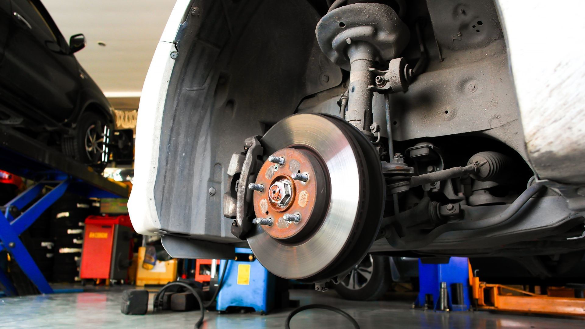 Car wheel with brake disc and caliper exposed for repair in a workshop.