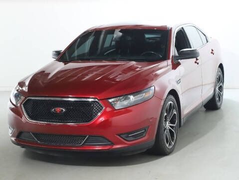 Red Ford Taurus sedan, black grille, sporty wheels, parked in a studio with white background.