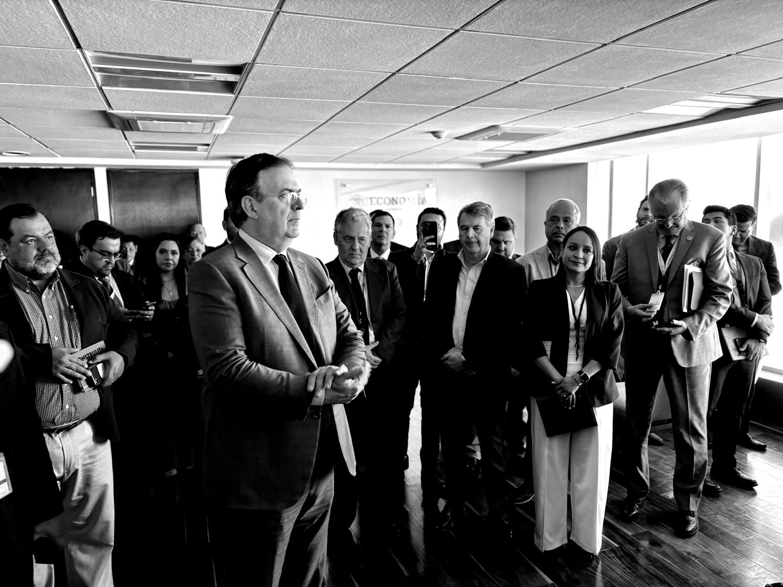 A group of people in a room, possibly an office. A man in a suit is speaking to the group.