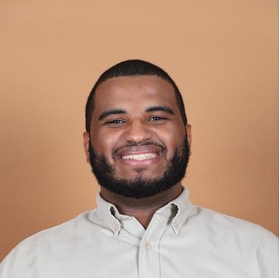 Smiling man with a beard in a light shirt against a tan background.