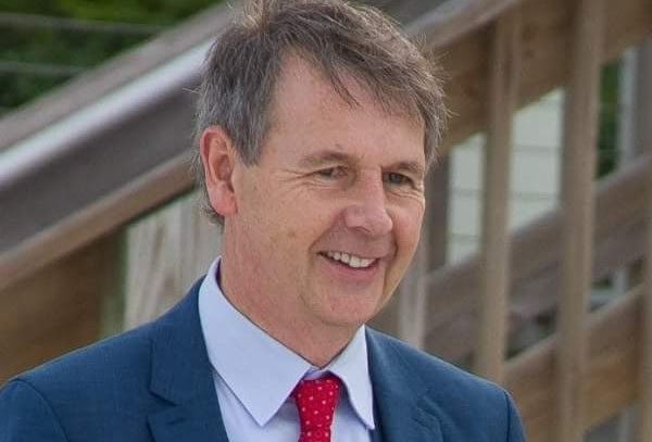 Smiling man in a blue suit and red tie, outdoors near wooden steps.