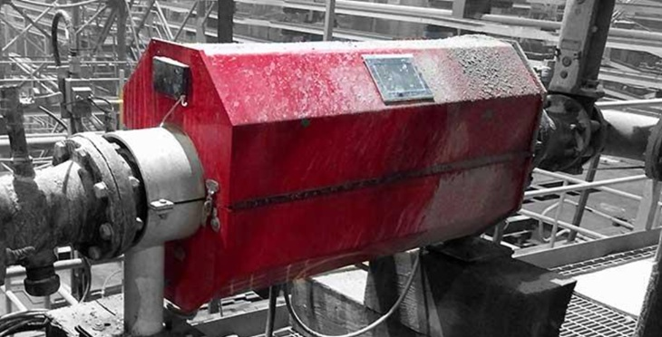 Red insulated valve cover on industrial pipes, with a small display and cables.  Outdoor setting, grayscale background.