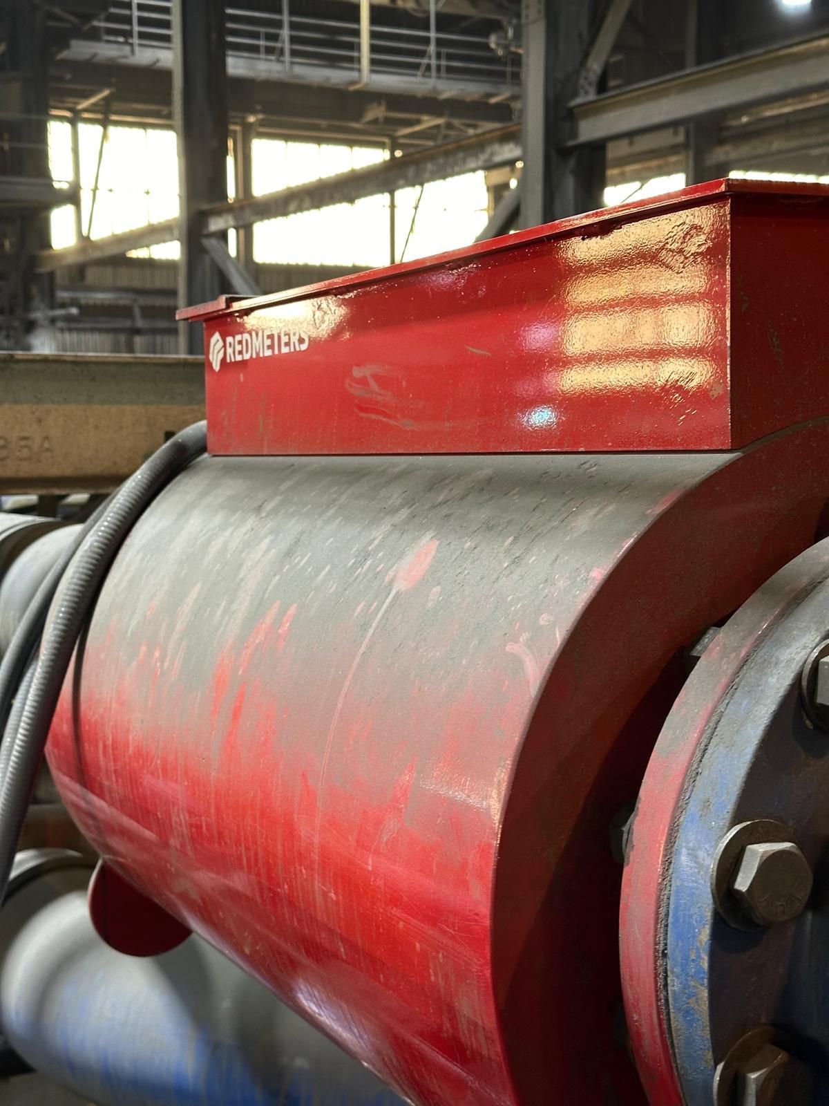 Red industrial equipment with a red rectangular box on top in a large factory setting.