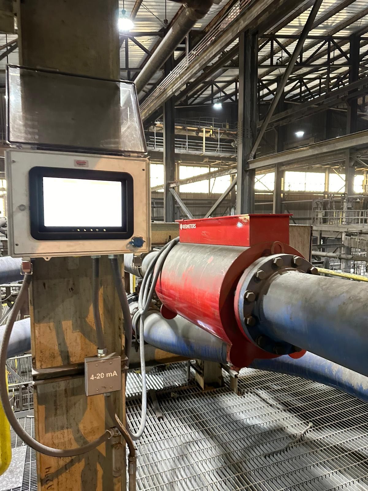 Red Meters Process Control System. A control panel with a screen attached to a pipe in an industrial setting. The pipe is red and blue.