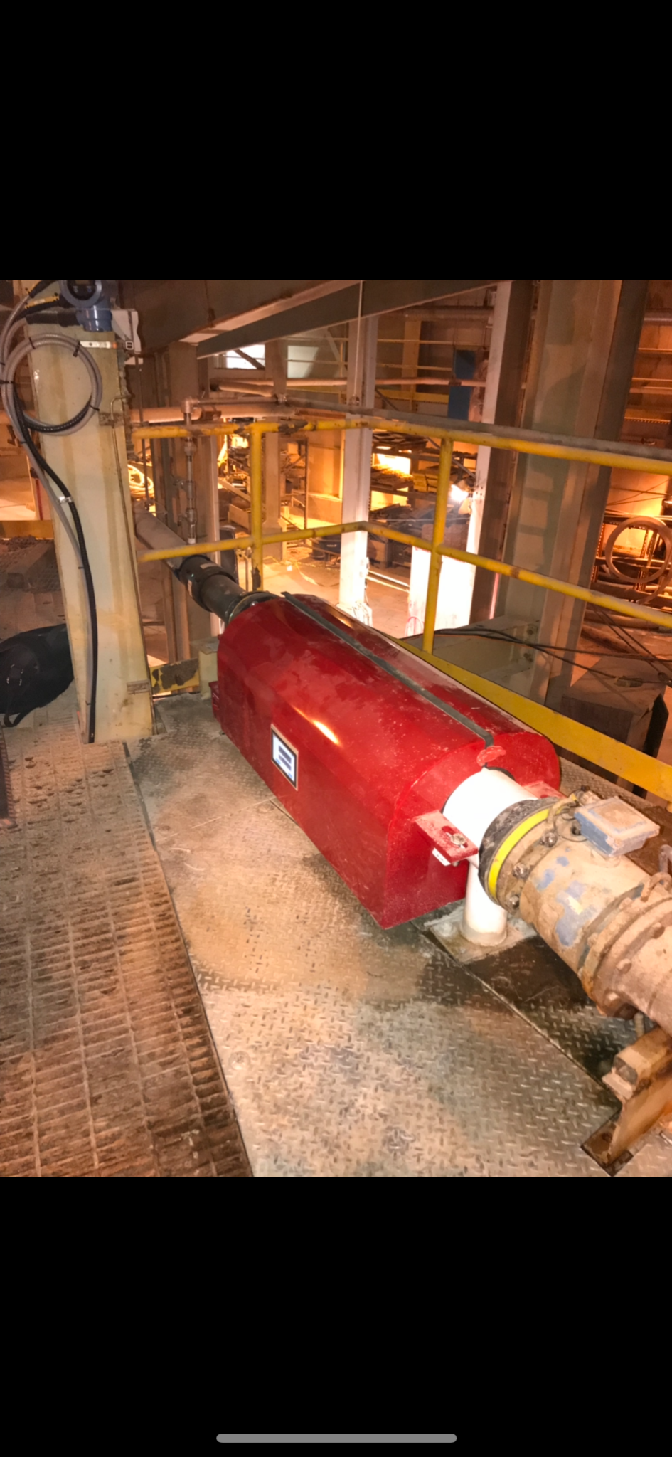 A red industrial filter connected to pipes in a factory setting. Yellow handrails and metal grating are visible.