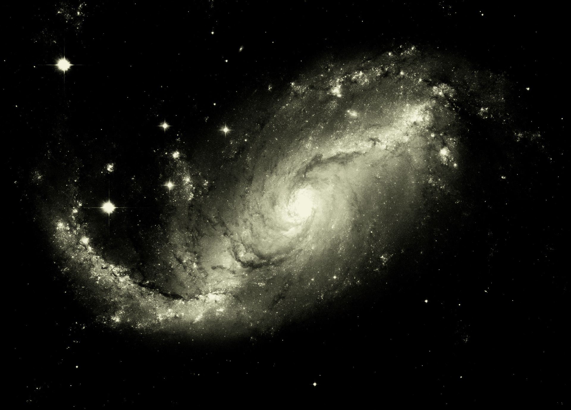 A spiral galaxy, appearing in shades of sepia, with bright spiral arms, a central bulge, and scattered stars against a black background.