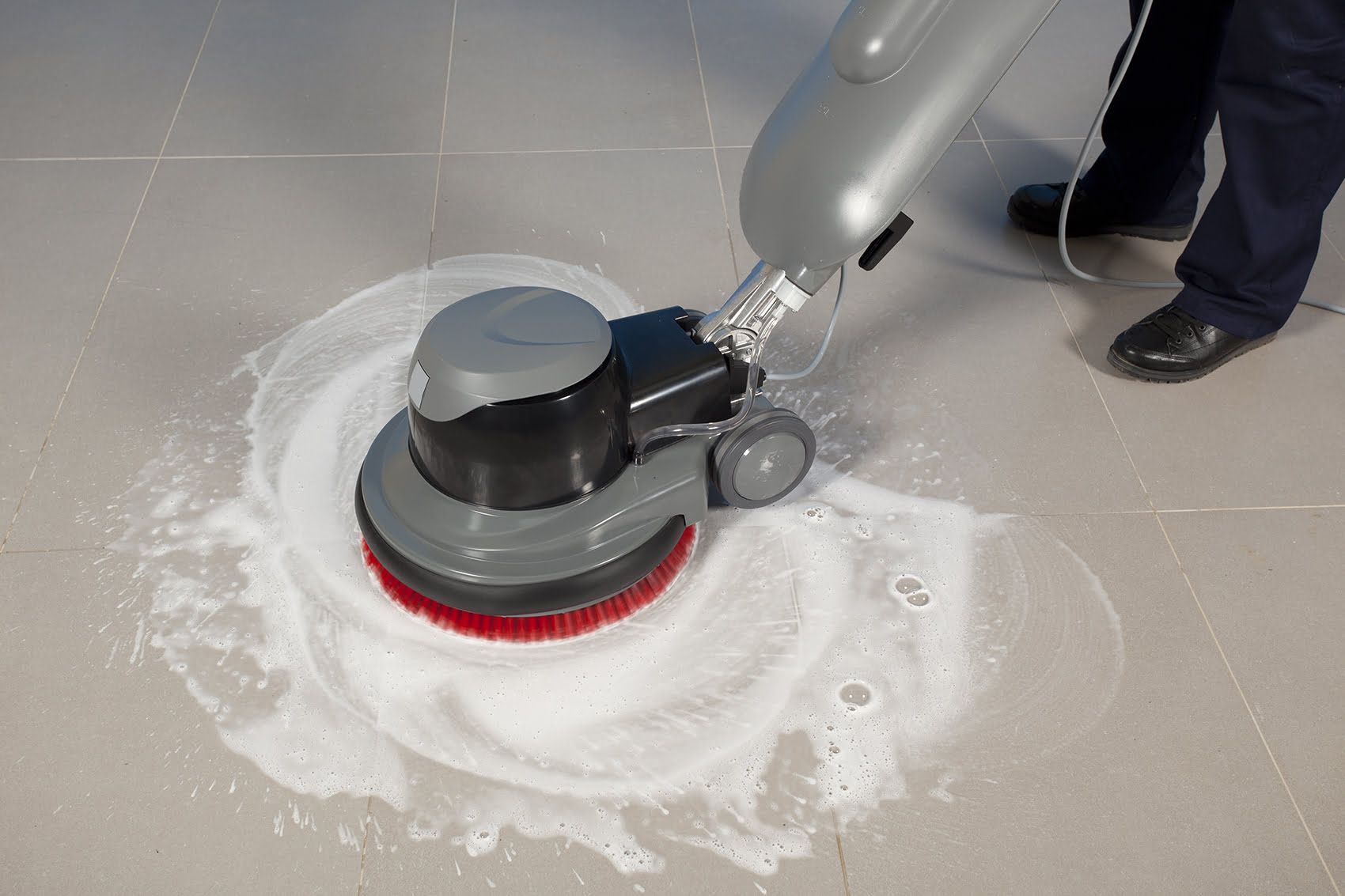 Floor cleaning machine scrubbing tile floor with white cleaning solution.