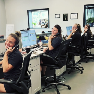 Customer service agents in black chairs smiling at desks with computer monitors in an office