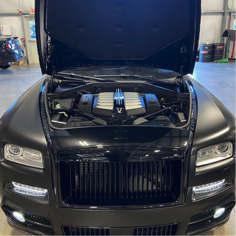 Black Rolls-Royce with hood open, showing exposed engine in a garage