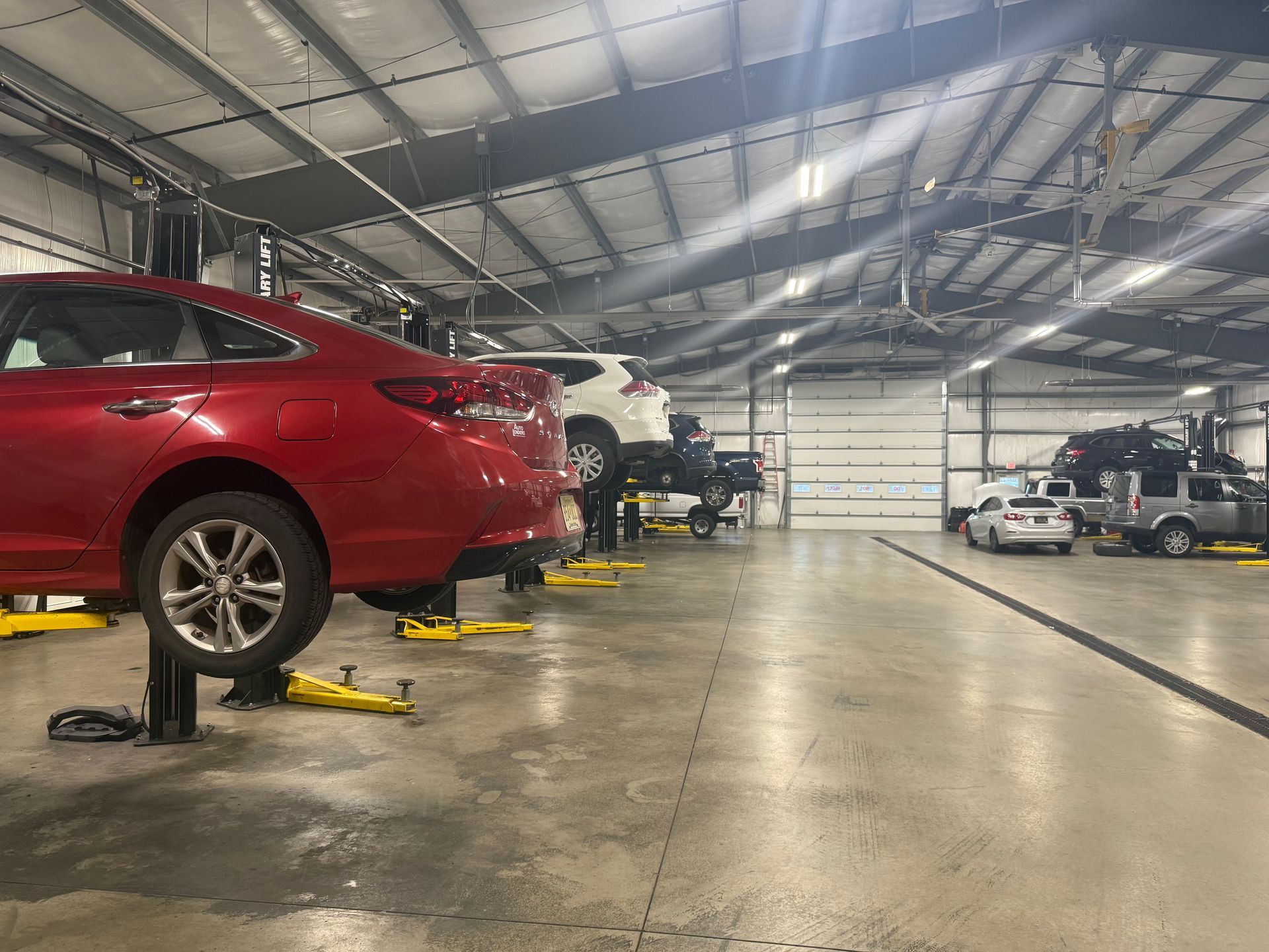 Auto repair shop with cars lifted on jacks, including a red sedan in the foreground.