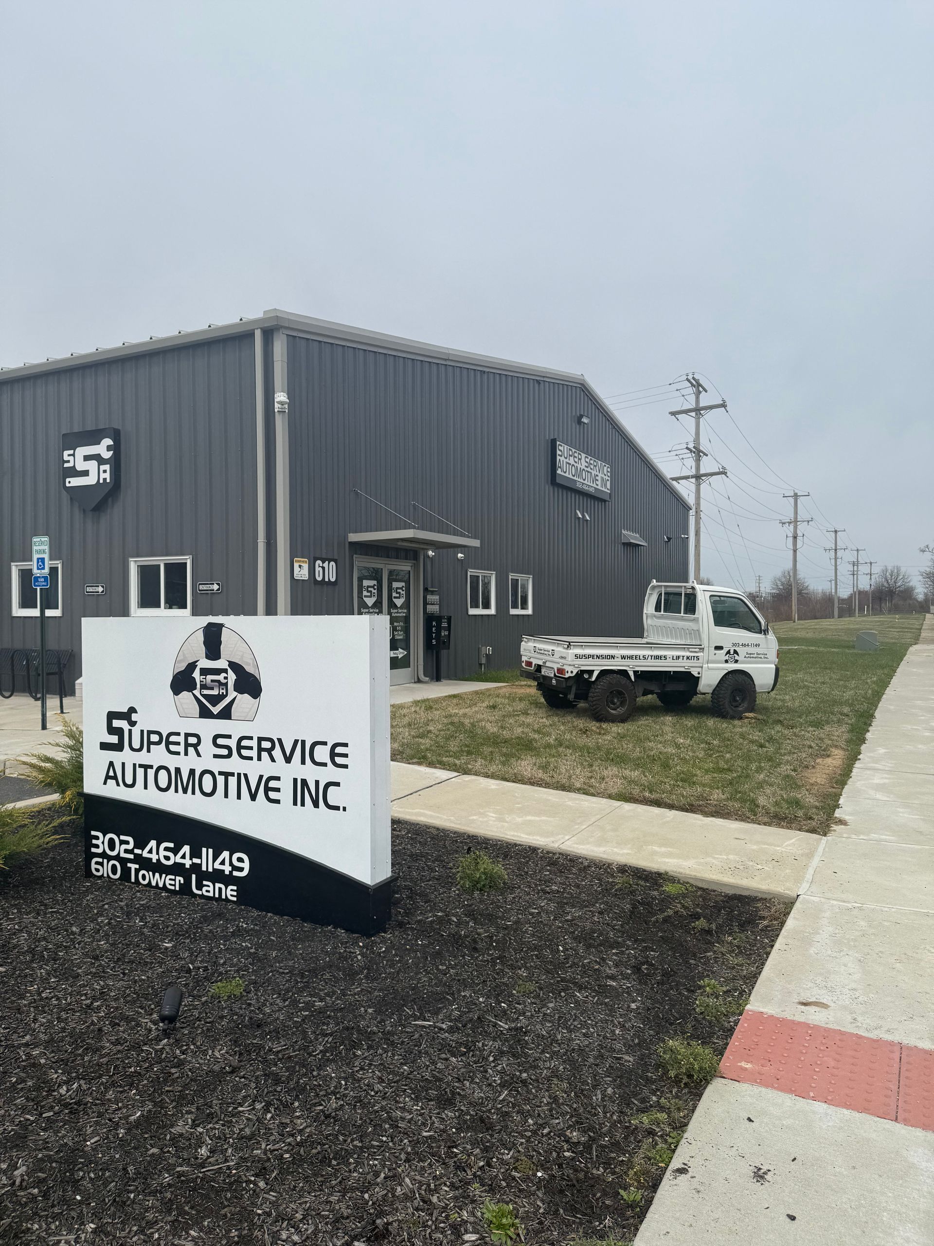 Super Service Automotive Inc. building with sign, parked white SUV, and sidewalk on a cloudy day