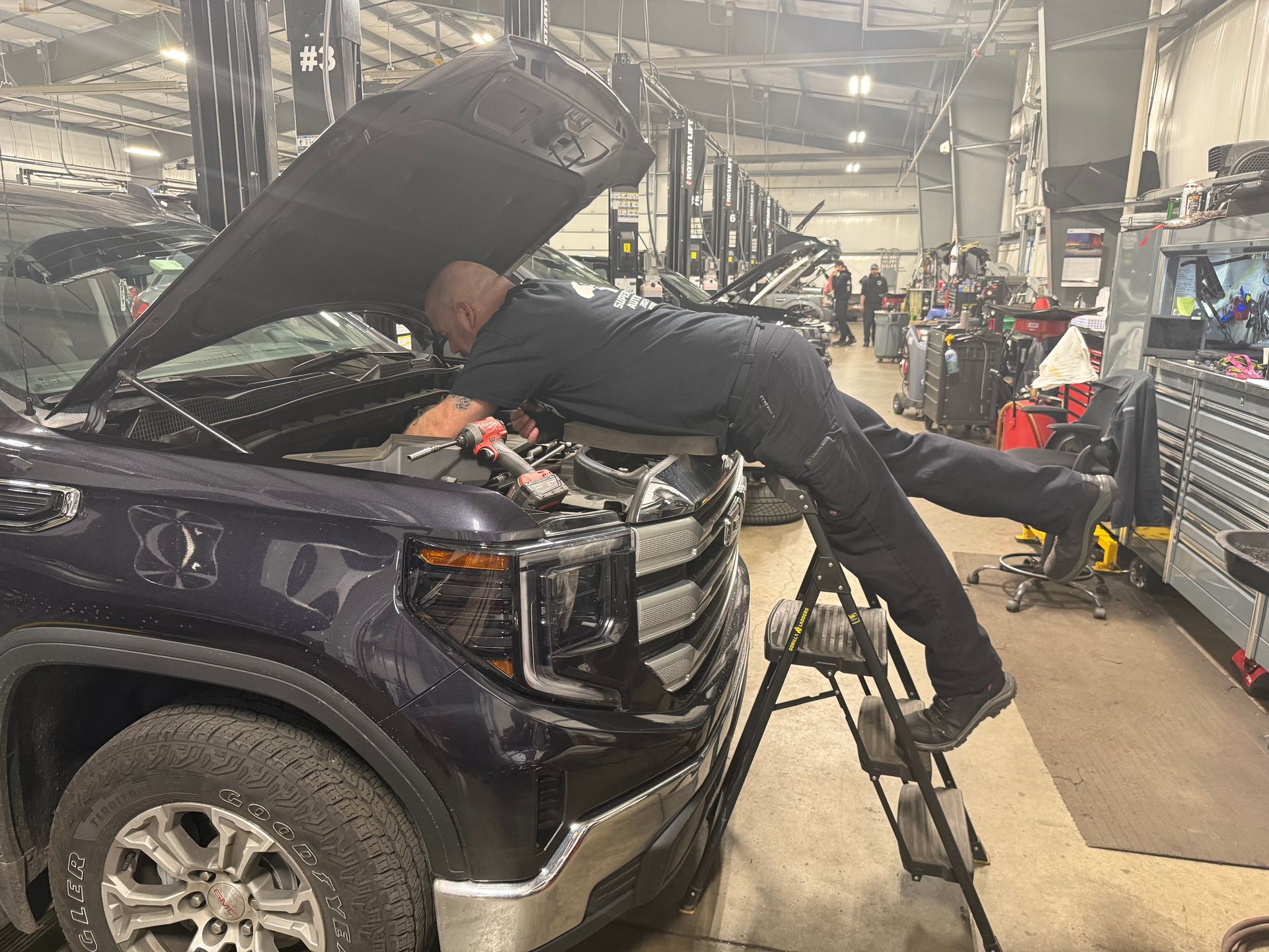 Mechanic leaning into a dark SUV with hood open inside an auto repair shop