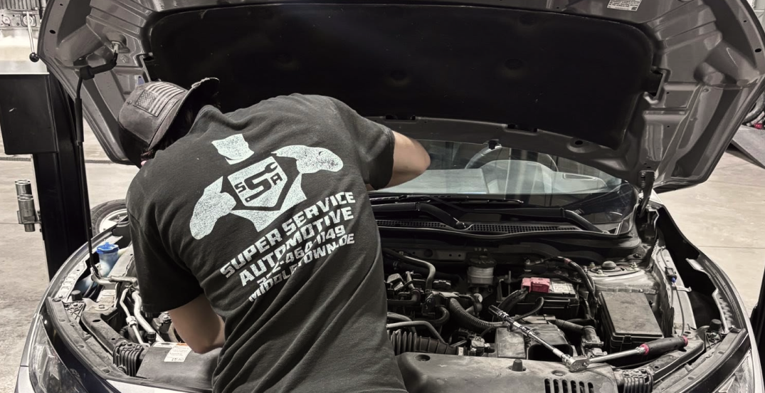 Mechanic working under a car’s open hood in a garage, inspecting the engine bay
