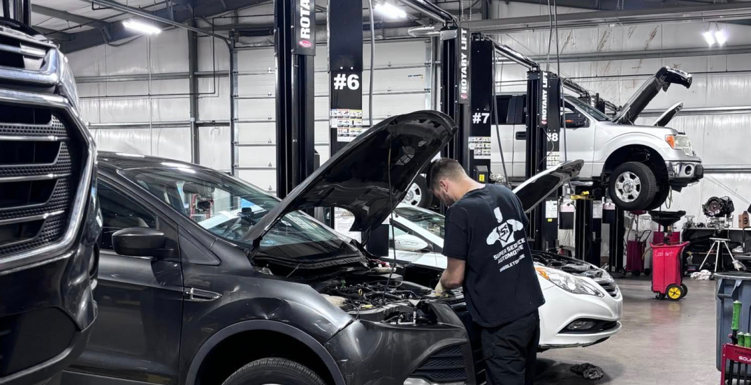 Mechanic working on a black SUV in an auto repair shop with cars on lifts nearby