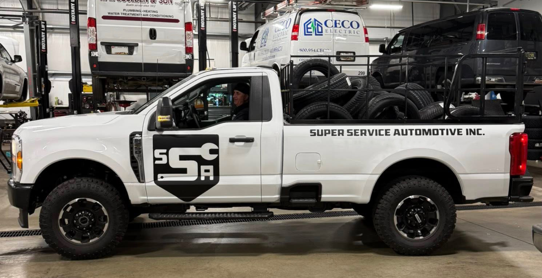 White service pickup truck with black logo decals parked inside an auto shop garage.