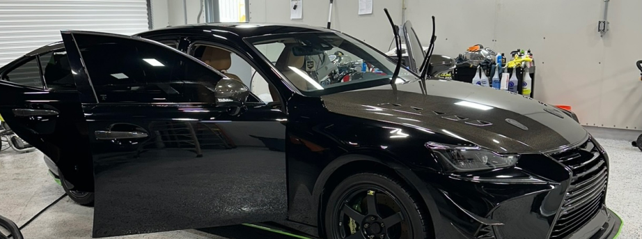 Black sedan with driver-side door open inside a garage or auto shop