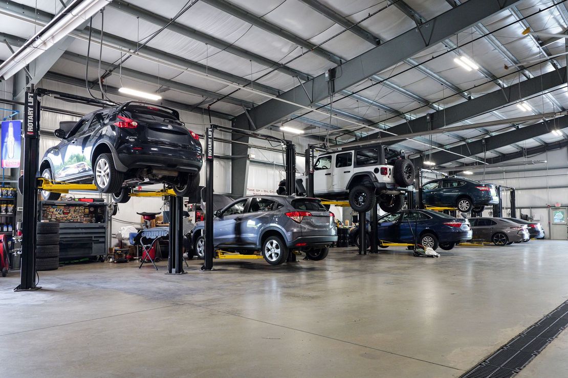 Auto repair shop with several cars on lifts inside a large service bay.