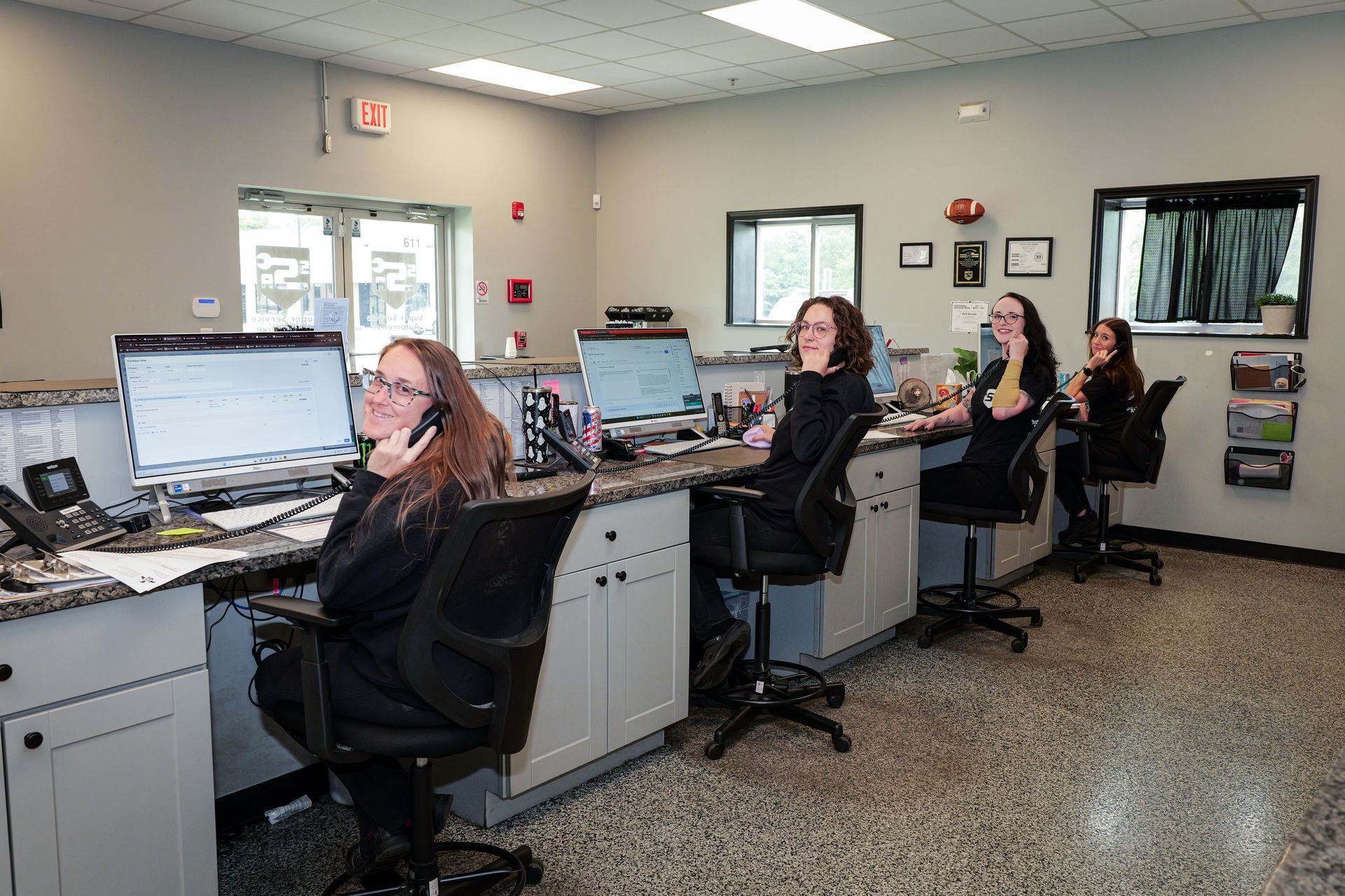 Customer service agents in black chairs smiling at desks with computer monitors in an office