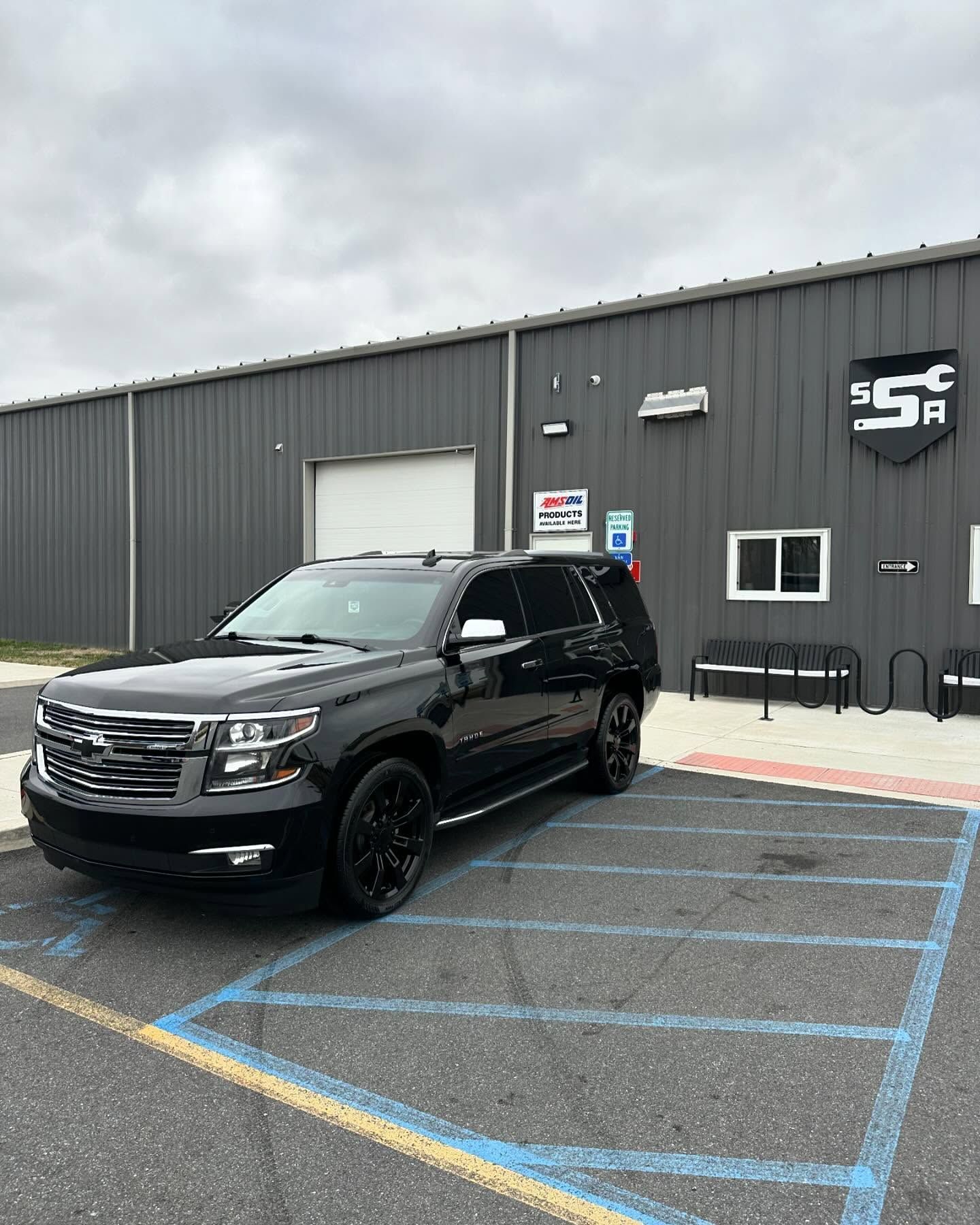 Black SUV parked in a blue-lined accessible space beside a gray building.